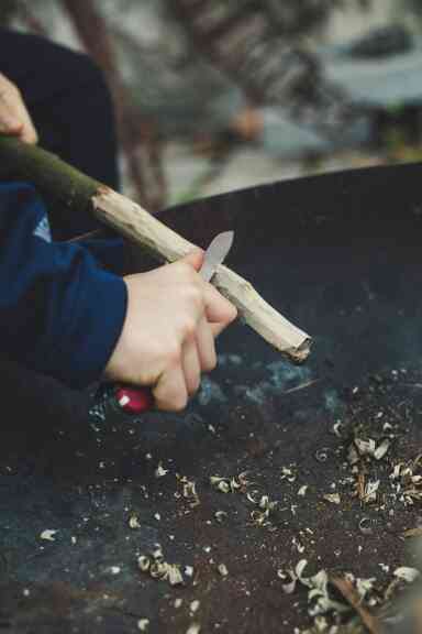 A hand carving a piece of wood with a pen knife